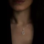گردنبند نقره طرح راکت تنیس روی گردن زن با پس‌زمینه تیره و استایل مینیمال