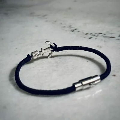 نمای کامل دستبند لنگر نقره با بند نخی مشکی و قفل مگنتی روی سطح سنگی